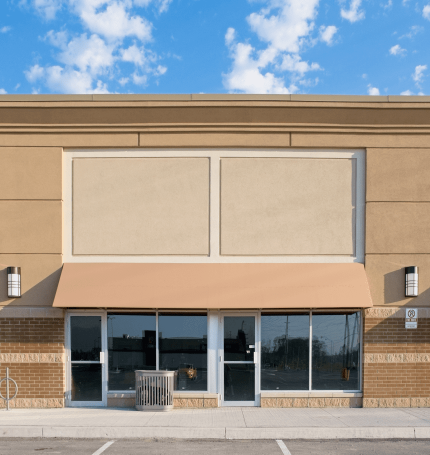 Empty storefront, beige building, sunny day.